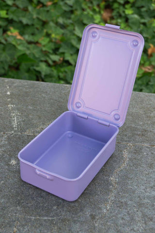 Purple storage box with lid on a stone surface with green foliage in the background