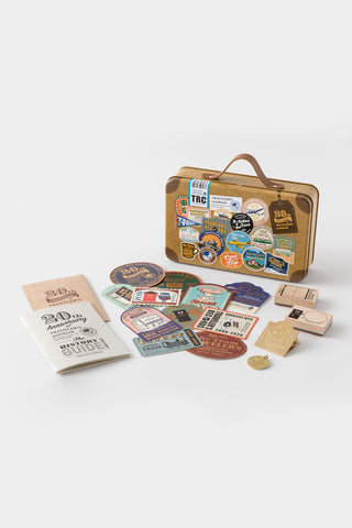 Travel-themed set with mini suitcase, stickers, and book on a white background