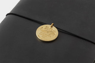 Black leather notebook with a gold tag featuring text on a light gray background