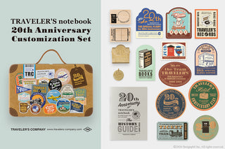 Traveler's notebook 20th Anniversary Customization Set with stickers and a suitcase on a light gray background.