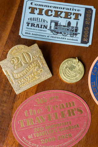 Collection of commemorative items including a ticket, stamp, and charm on a wooden surface.