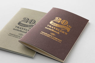 Two notebooks, one beige and one brown, with '20th Anniversary Traveler's Company' branding on a light gray background.
