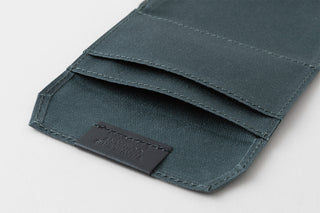 Close-up of a teal fabric wallet with a brand label on a light gray background