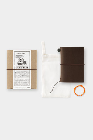 Brown leather notebook, cardboard packaging with text, and orange band on a white background