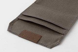 Close-up of a brown fabric pouch with a visible brand label on a light gray background