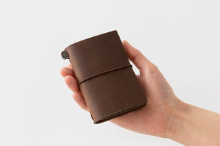 Hand holding a brown leather notebook against a white background