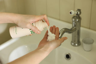 Hands dispensing cleanser from a beige pump bottle at a sink