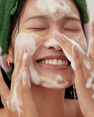 Person applying white cleanser foam around eyes and cheeks