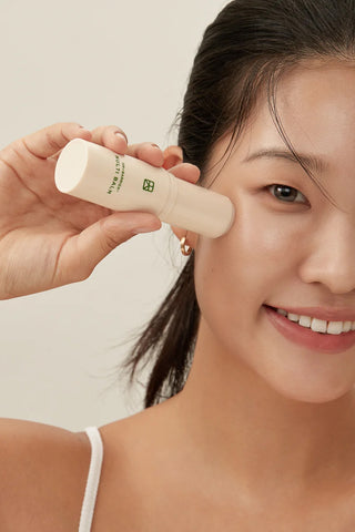 Person applying Multi Balm stick near ear; beige tube held in hand