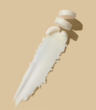 White balm swatch on flat surface with beige balm tube and cap