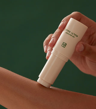 Multi balm stick held in hand over forearm; beige tube with green mark
