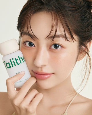 Talitha Koum essence soo bottle held near face, white cap and green label