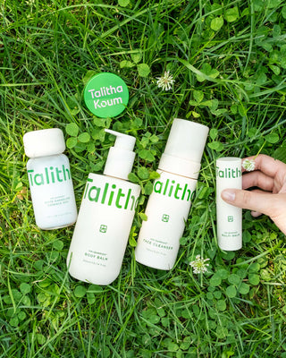 Talitha Koum lipcure balm tin on grass with white skincare bottles nearby