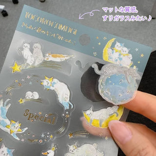 Sticker sheet with cat designs and a hand holding a clear sticker.