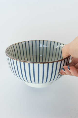 Hand holding a ceramic bowl with blue stripes on a white background