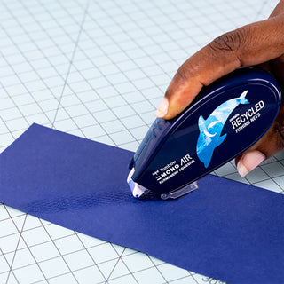 Hand using a blue paper trimmer on a blue sheet of paper with a grid background