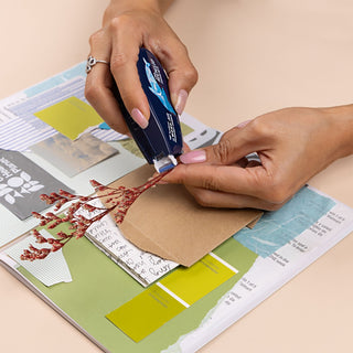 Person using a glue tape on a design project with color swatches and plant stem.
