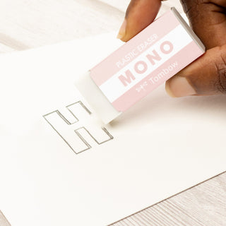 Hand holding a pink and white eraser labeled 'MONO' over a piece of paper with cut-out letters.