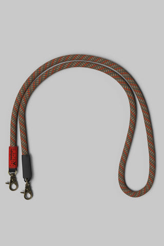 A braided rope bag strap with a red and brown pattern, featuring bronze metal clasps on a solid gray background.