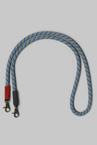 A braided rope bag strap with a blue, yellow, and white pattern, with bronze hardware on a neutral gray background.