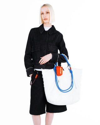 Person wearing a black jacket and holding a white bag with blue straps on a white background