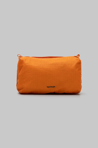 An orange waterproof bag with a small black 'topologie' logo on the front, against a solid gray background.