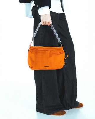 Person holding an orange handbag with a braided strap on a white background