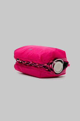 Bright pink sacoche bag laying down with water bottle inside against a light gray background
