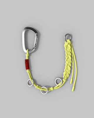 A yellow braided rope carabiner lanyard with silver metal hardware, including a carabiner, rings, and a red branded tag, shown on a solid gray background.
