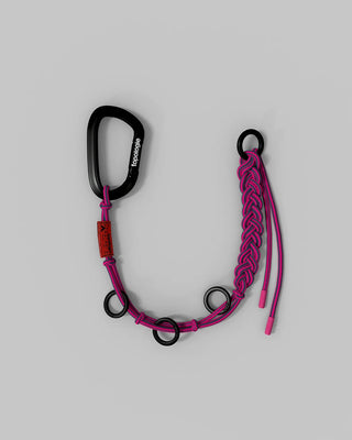 A pink and black carabiner accessory with a black carabiner, pink braided cord, and black metal rings, displayed on a neutral gray background.