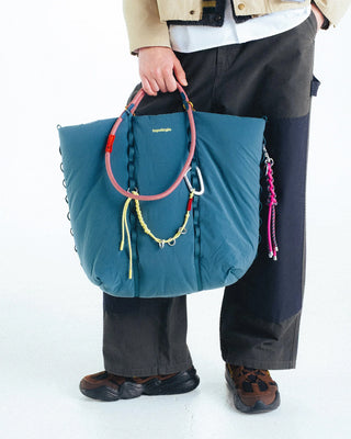 Person holding large blue bag with multiple straps and keychain attatched 