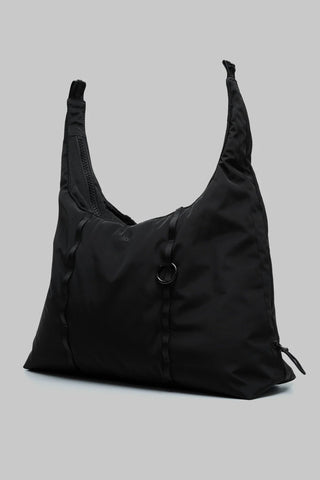 A  medium black slouchy shoulder bag featuring a circular metal ring detail on the front, photographed on a solid gray background.