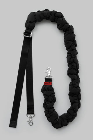 A black padded bag strap with silver metal hardware, displayed on a neutral gray background.