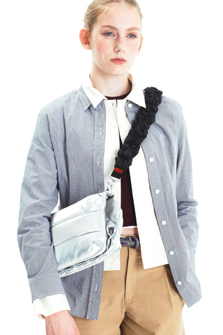 A model wearing a blue and white striped button-up carrying a shiny silver puffer bag with a black padded shoulder strap.