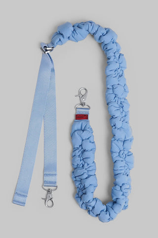 A light blue padded bag strap featuring silver metal hardware, on a neutral gray background.