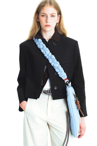 A model wearing a black jacket and white pants carrying a light blue puffer tote with a light blue padded crossbody strap.