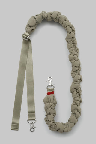 A beige padded bag strap with silver hardware shown on a solid gray background.