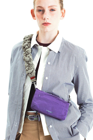 A model wearing a gray and white striped button-up shirt carrying a purple crossbody bag with a chunky padded grey strap.