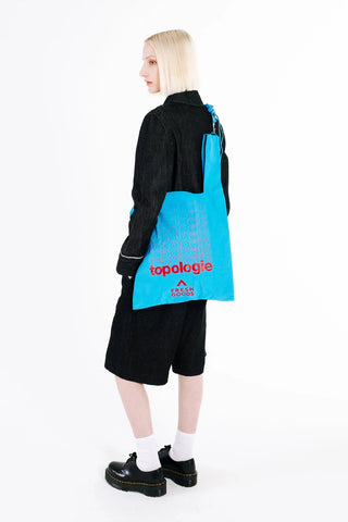 Person wearing a blue tote bag with 'topologie' branding on a white background