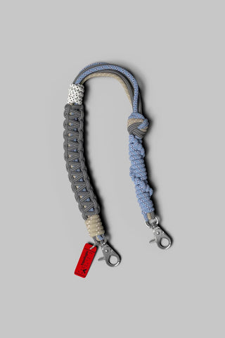 A grey and pale blue braided rope wrist strap with silver hardware on a light grey background