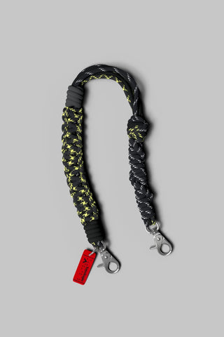 A braided black and yellow rope wrist strap with silver metal lobster clamps and on a plain light gray background.