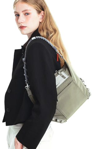 A person carrying a green bag over her shoulder with a grey braided rope strap on a white background