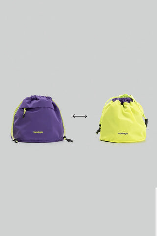 Purple and yellow reversible drawstring bags with a brand logo on a gray background