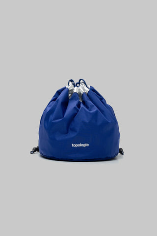 Blue drawstring bag with 'topologie' branding on a gray background