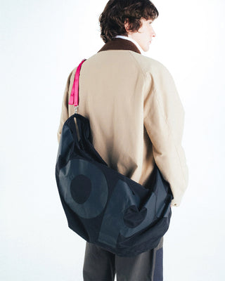 Person wearing a large black bag with a visible brand logo with a bright pink strap on a white background