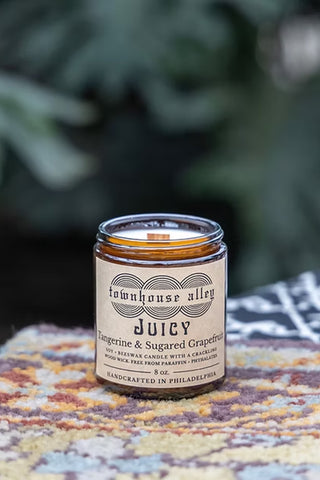 Candle jar labeled 'townhouse alley Juicy' on a textured surface with a blurred green background