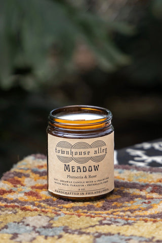 Candle in a glass jar with a label on a textured surface with blurred greenery in the background