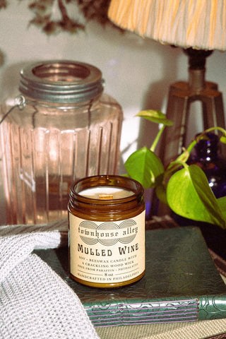 Candle labeled 'Townhouse Alley Mulled Wine' on a surface with decorative items in the background.