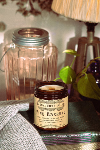 Jarred candle labeled 'Pine Barrens' from 'Townhouse Alley' on a surface with decorative items.