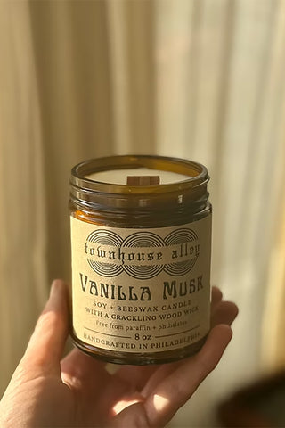 Hand holding a candle labeled 'Vanilla Musk' from 'townhouse Alley' against a neutral background.